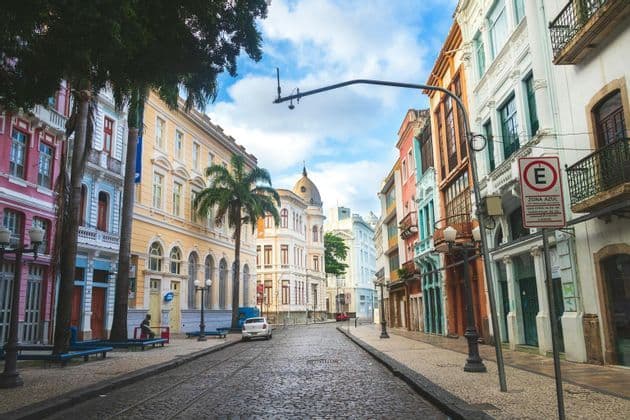 Una strada acciottolata con binari del tram è fiancheggiata da edifici colorati in stile coloniale e palme sotto un cielo azzurro.