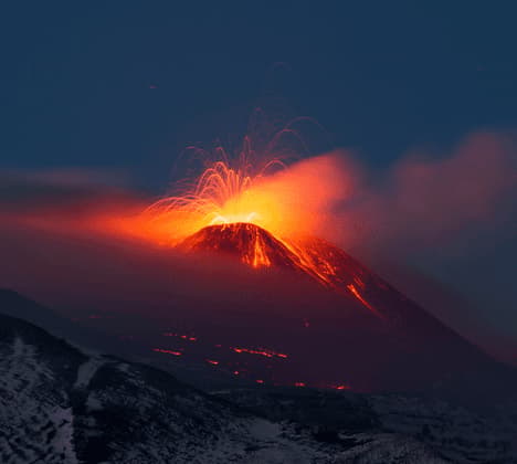 Un vulcano che erutta di notte, proiettando una pioggia di lava incandescente e scintille nel cielo scuro.
