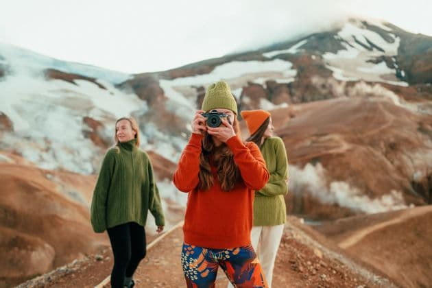 Eine Frau auf einer WeRoad-Gruppenreise fotografiert mit zwei anderen Frauen in einer geothermischen Landschaft.