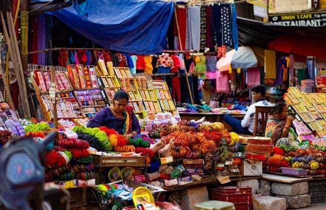 Une femme vend des joncs et des bracelets colorés sur son stand dans un marché de rue animé et en plein air.