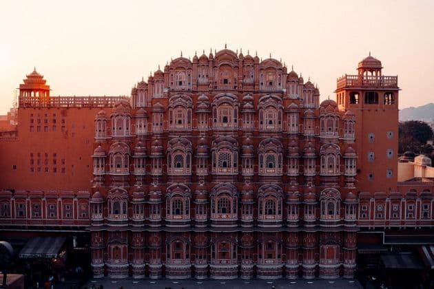 La facciata simmetrica di un sontuoso palazzo rosa-rossastro, con numerose piccole finestre dettagliate, sotto un cielo al tramonto pallido.