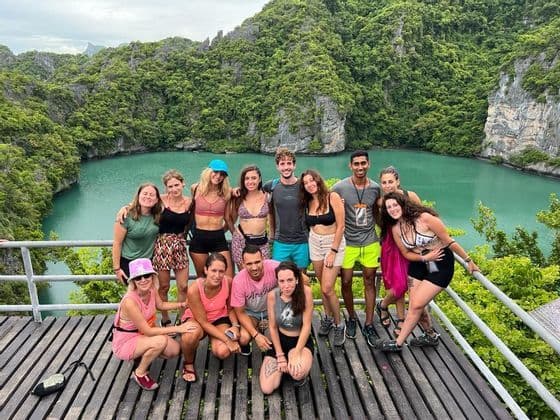 Un groupe WeRoad pose pour une photo sur un point de vue en bois surplombant un lagon turquoise entouré de falaises verdoyantes.