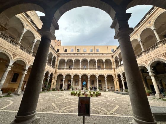 Cortile di un edificio storico con colonnati ad arco, inquadrato tra due grandi colonne in primo piano sotto un arco.
