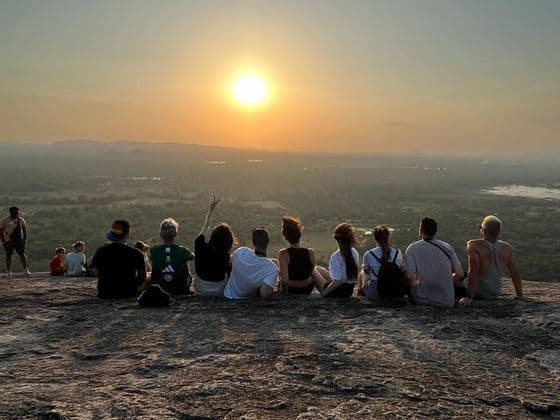 Un gruppo WeRoad ammira il tramonto da una collina rocciosa su un vasto paesaggio verde.