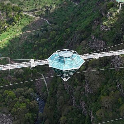 Une vue aérienne d'une structure en verre en forme de diamant sur un pont suspendu enjambant un canyon profond et verdoyant.