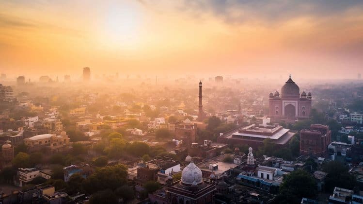 Una vista aérea de una mezquita histórica y un minarete en una ciudad densa, envuelta en un amanecer dorado y brumoso.