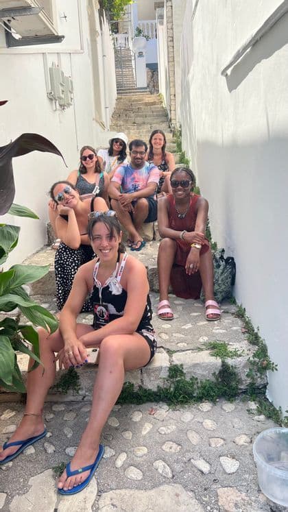 Un voyage en groupe WeRoad de sept personnes souriantes, assises ensemble sur un étroit escalier extérieur en pierre.