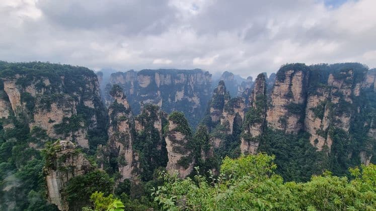 Un vasto paesaggio di imponenti formazioni rocciose a pilastro, coperte da alberi verdi e vegetazione, sotto un cielo nuvoloso.