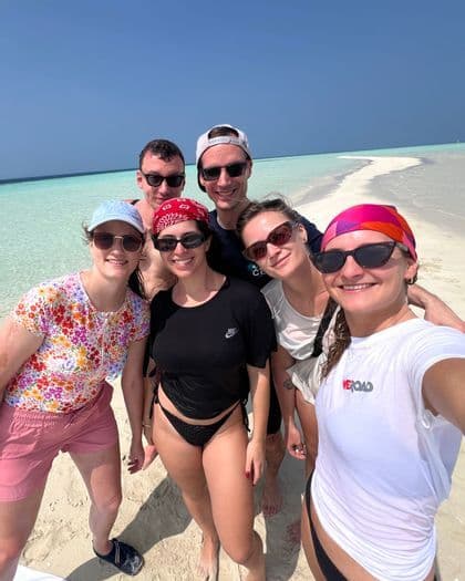 Eine WeRoad Gruppenreise von sechs Personen, die für ein Selfie auf einer weißen Sandbank neben türkisblauem Wasser unter einem klaren blauen Himmel lächeln.