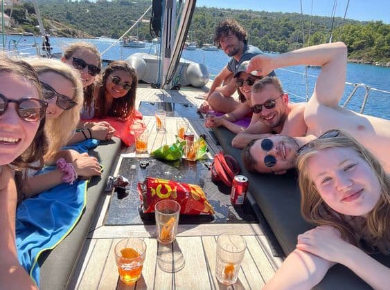 Eine WeRoad Gruppenreise von lächelnden und entspannten Menschen auf dem Deck eines Segelboots mit Getränken und Snacks an einem sonnigen Tag.