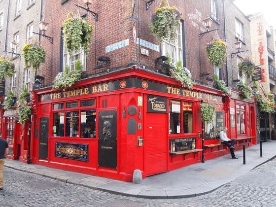 L'esterno del pub The Temple Bar, con la sua vivace facciata rossa su un angolo di strada acciottolata e cesti di fiori appesi.