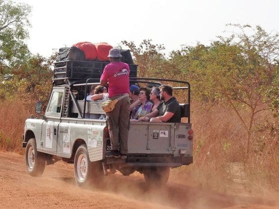 Un gruppo WeRoad a bordo di una jeep da safari, solleva polvere su una strada sterrata attraverso la savana, con una guida.