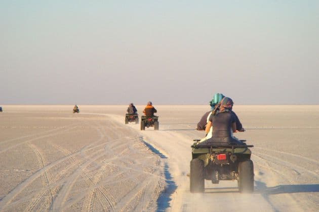 Eine WeRoad-Gruppe fährt auf Quads in einer Reihe durch eine weite, weiße Wüstenlandschaft unter klarem Himmel.