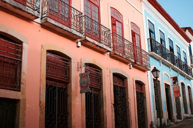 Un bâtiment colonial rose aux fenêtres rouges se dresse à côté d'un bleu, tous deux ornés de balcons en fer forgé.
