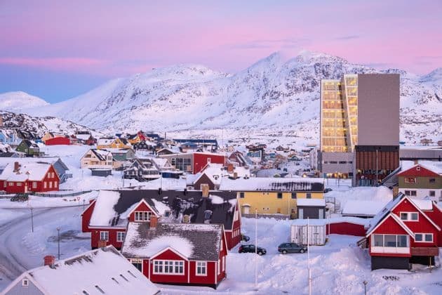 Case colorate in una città innevata ai piedi di grandi montagne sotto un cielo rosa.