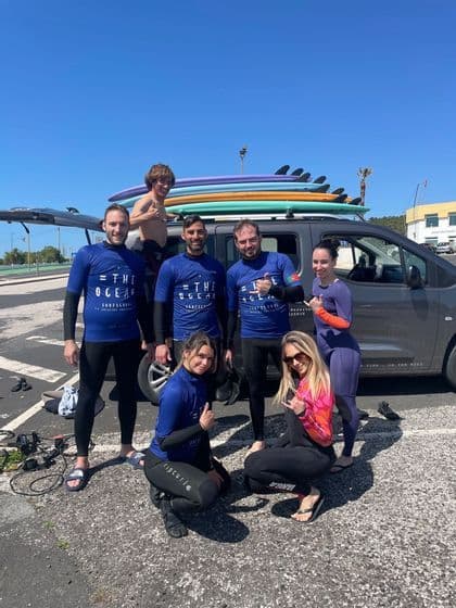 Un viaggio di gruppo WeRoad di persone in muta che posano per una foto davanti a un furgone con tavole da surf sul tetto.