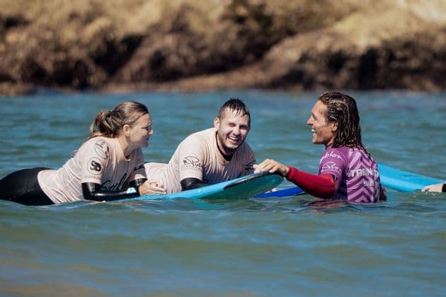 Tre persone di un gruppo WeRoad che ridono in acqua con le loro tavole da surf durante una lezione di surf.