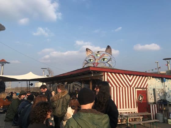 Un viaggio di gruppo WeRoad si riunisce in un luogo all'aperto con una grande scultura di gatto a tre occhi sul tetto a strisce.