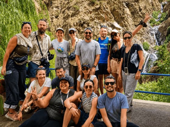 Un grupo de WeRoad sonriendo y posando para una foto frente a una montaña rocosa y una cascada.
