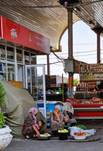 Tre donne con foulard tradizionali vendono mele da secchi in un mercato all'aperto.