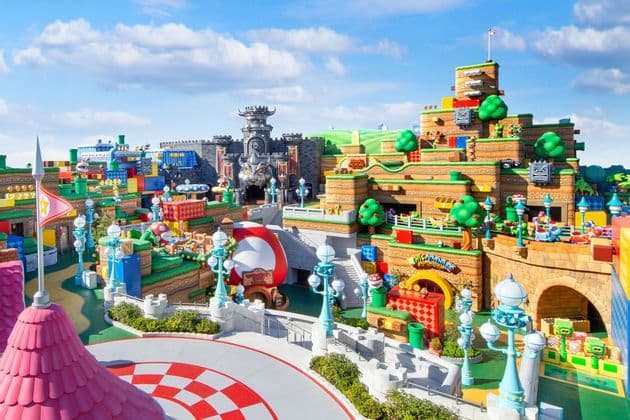 Una panoramica colorata del parco a tema Super Nintendo World, con castelli iconici, tubi verdi e strutture a blocchi sotto un cielo soleggiato.