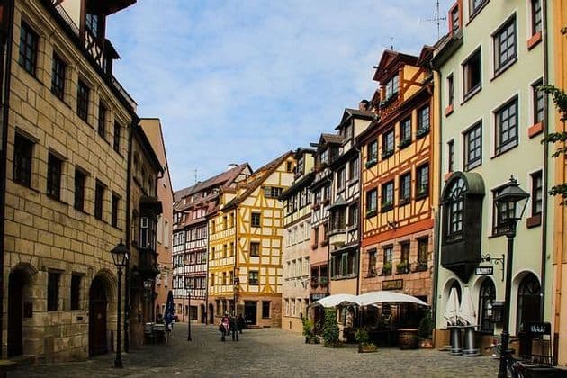 Una strada acciottolata curva tra file di colorati e storici edifici a graticcio sotto un cielo parzialmente nuvoloso.