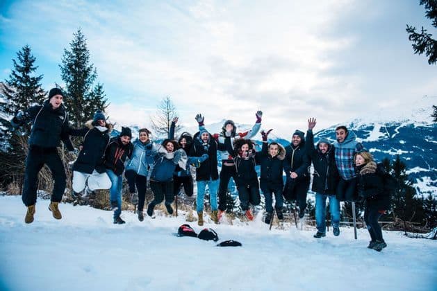 Eine WeRoad Gruppenreise von Menschen in Winterkleidung, die gemeinsam an einem verschneiten Berghang springen.