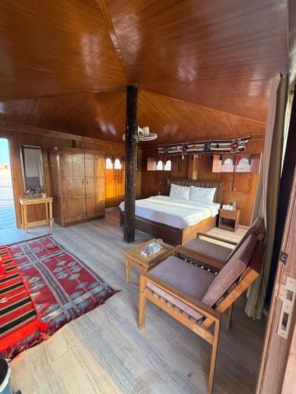L'interno di una spaziosa tenda-camera con pannelli in legno, dotata di un letto matrimoniale, mobili in legno e tappeti rossi a fantasia.