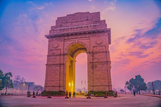 L'India Gate, un imponente arco in pietra, è illuminato contro un cielo rosa e viola dai colori vivaci all'alba.