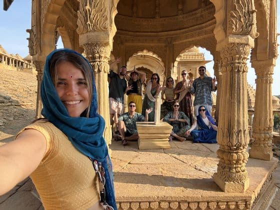 Una donna con un foulard blu si fa un selfie con il suo gruppo WeRoad all'interno di un padiglione in arenaria riccamente decorato.