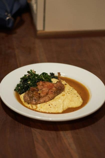 Coscia di pollame arrosto con sugo servita su un letto di polenta cremosa con un contorno di verdure saltate.