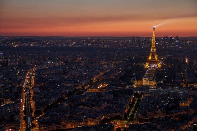 Una torre a traliccio illuminata che si erge su un paesaggio urbano luminoso al crepuscolo sotto un cielo arancione