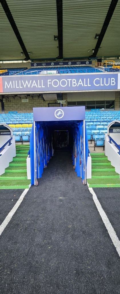 Un tunnel blu estendibile per i giocatori che porta in campo in uno stadio di calcio con seggiolini blu vuoti per gli spettatori