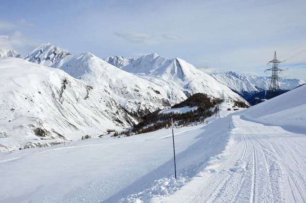 Una pista da sci battuta si snoda lungo creste montuose innevate sotto un cielo limpido con linee elettriche in lontananza