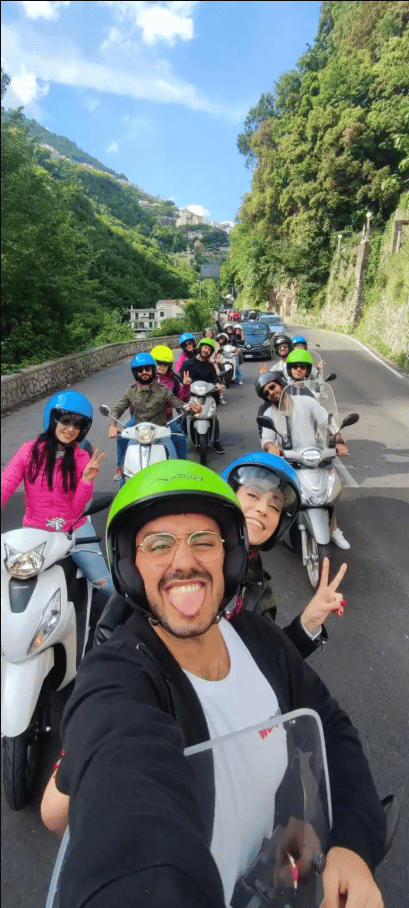 Un viaje en grupo de WeRoad en motonetas por una carretera sinuosa con cascos coloridos y sonriendo