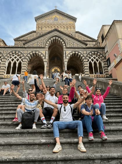 Un viaje en grupo de WeRoad sentado en escalones de piedra y saludando frente a una gran catedral