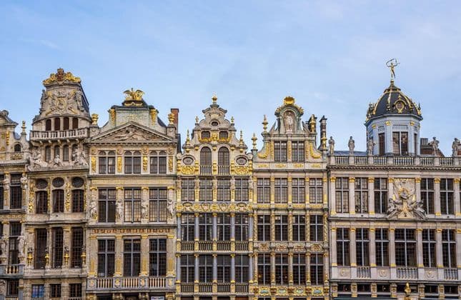 Facciate di edifici storici decorate con ornamenti dorati e statue sotto un cielo azzurro pallido.
