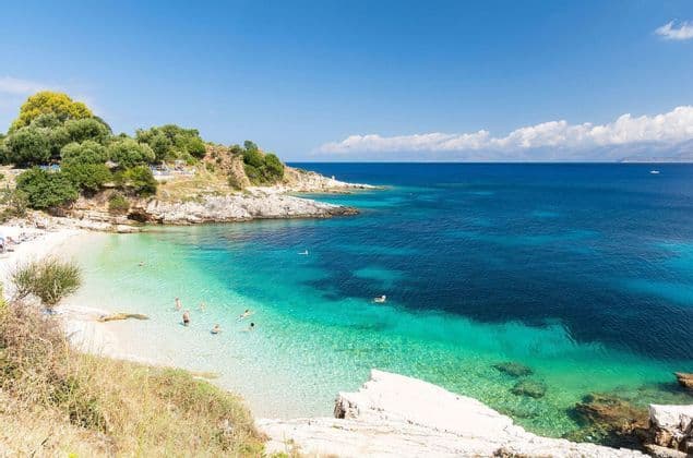 A high-angle view of a secluded cove with people swimming in the clear turquoise water next to a white sand beach.