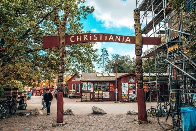 Der Eingang zu Christiania ist durch ein großes rotes Schild gekennzeichnet, das von zwei hohen, geschnitzten hölzernen Totempfählen mit Gesichtern gehalten wird.