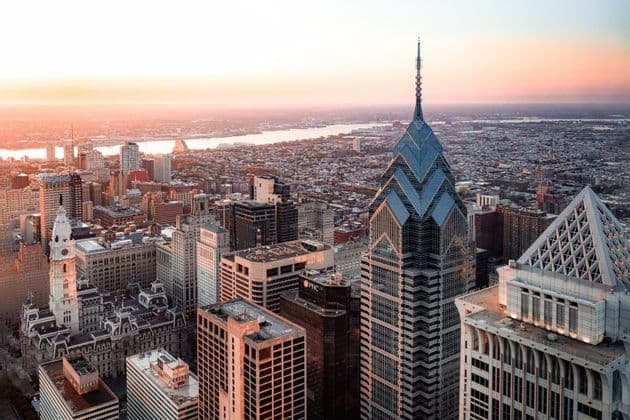 An aerial view of a sprawling city skyline with modern skyscrapers and a wide river illuminated by the warm light of sunrise.