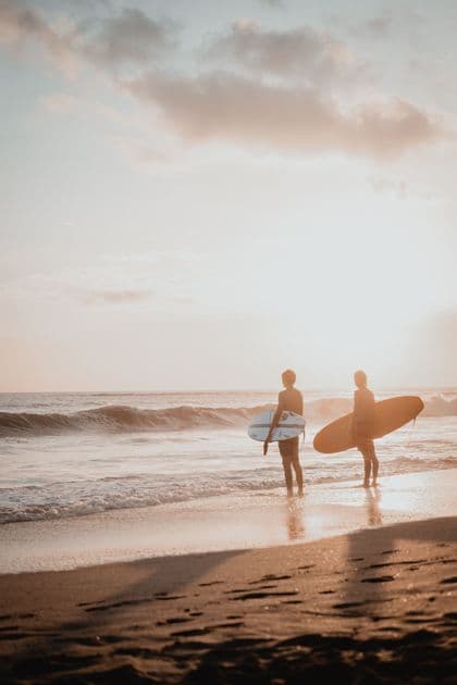 Dos surfistas con sus tablas de surf de pie en el agua poco profunda del océano al atardecer.