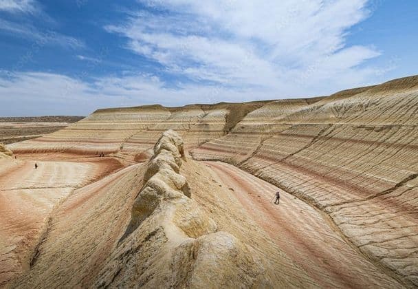 Un viaggio di gruppo WeRoad in escursione attraverso un vasto paesaggio di colline colorate e striate sotto un cielo parzialmente nuvoloso.