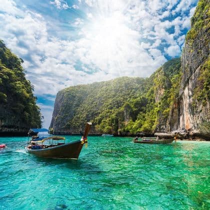 Hölzerne Longtail-Boote schwimmen auf türkisem Wasser in einer sonnigen Lagune, umgeben von üppig grünen Klippen.