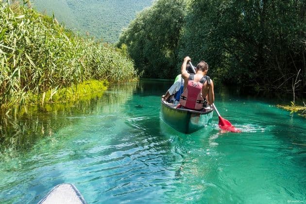 Un viaggio di gruppo WeRoad pagaia in canoa lungo un fiume limpido e turchese, fiancheggiato da alte canne verdi e alberi.
