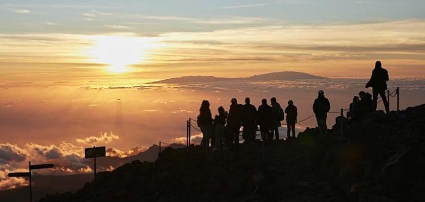 Un viaggio di gruppo WeRoad in silhouette su una cima di montagna che osserva il sole sorgere sopra un mare di nuvole.