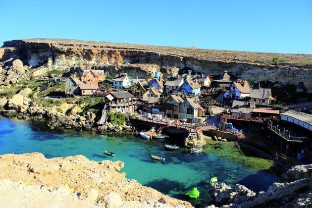 Un pueblo colorido de casas rústicas construido en una cala rocosa en una bahía con agua turquesa cristalina y pequeños barcos.