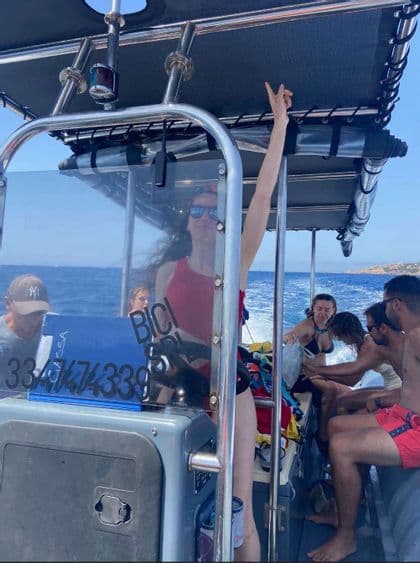 Un viaje en grupo de WeRoad en lancha, con una mujer en bañador rojo al timón haciendo el signo de la paz.