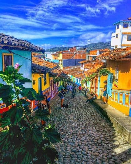 Una veduta dall'alto di una strada acciottolata in pendenza, fiancheggiata da edifici dai colori vivaci, con persone che passeggiano sotto un cielo azzurro.