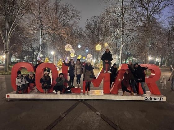 A WeRoad group trip poses for a photo on and around large, red letters in a park at night, illuminated by festive lights.