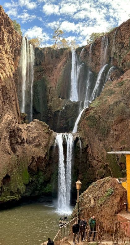 Un gruppo WeRoad a un punto panoramico ammira grandi cascate che scendono da scogliere rosse sotto un cielo parzialmente nuvoloso.